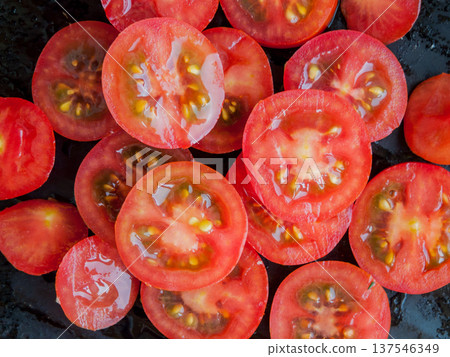 Seasonal diet. Bunch of sliced fresh red cherry tomatoes on black background, top view. 137546349