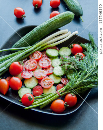 Fresh red cherry tomatoes, green leek and cucumber in pan on black background, top view. 137546350