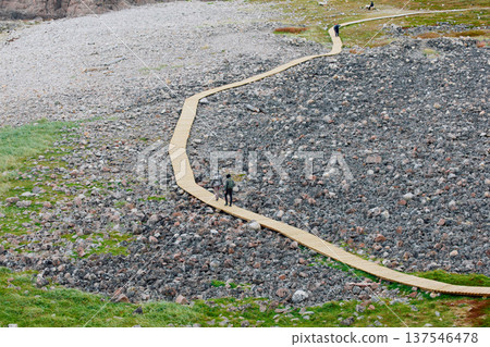Russia, Teriberka, People walk along a wooden path at sunset, the coast of the Barents Sea, the rocky shore with colourful arctic carpet of moss, yagel, Tundra at autumn, Murmansk 137546478