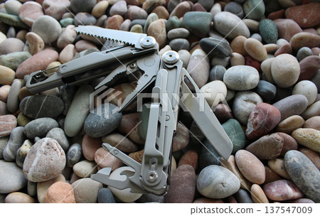 Half-opened full metal multi-tool with different blades and folding screwdrivers on colored pebbles Half-opened full metal multi-tool with different blades and folding screwdrivers on colored pebbles 137547009