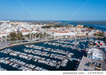Ria Formosa shows a busy dock filled with boats. Faro's Old Town can be seen in the background on a clear, sunny day in Algarve, Portugal Ria Formosa shows a busy dock filled with boats. Faro's Old Town can be seen in the background on a clear, sunny day in Algarve, Portugal 137547035