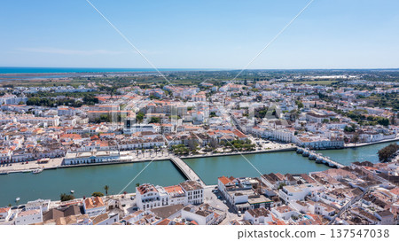 Tavira in Algarve is seen from above with traditional buildings lined along the Gilao river. The coastline and countryside can be observed in the distance Tavira in Algarve is seen from above with traditional buildings lined along the Gilao river. The coastline and countryside can be observed in the distance 137547038