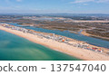 Aerial view shows Praia de Faro with people on the beach and Ria Formosa nearby. The coastline stretches as boats are visible in the water on a clear day 137547040