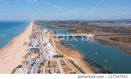 Aerial view captures Praia de Faro and Ria Formosa, displaying the beach, town, bridges, and water during a sunny day 137547041
