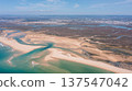 Drone captures the landscape of Ria Formosa and Praia de Faro in Portugal showing sandy beaches, water, and green areas under clear blue skies 137547042