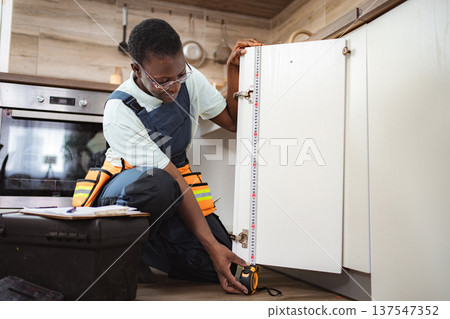 Handyman measuring kitchen cabinet door with tape measure 137547352