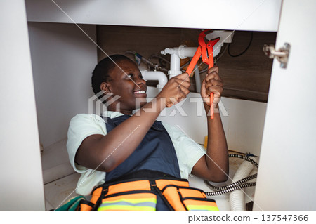 Plumber fixing pipes under kitchen sink using a wrench Plumber fixing pipes under kitchen sink using a wrench 137547366