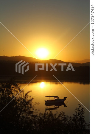 Small fishing boat with reflection in calm sea at sunrise. Small fishing boat with reflection in calm sea at sunrise. 137547454