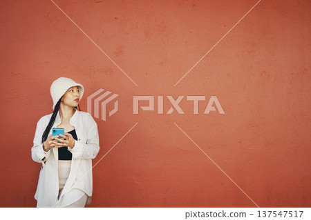 Thinking, wall and woman with phone in a city for travel, search or location map on orange background. Smartphone, app and lady fashion influencer outdoor on social media, blog, or podcast idea 137547517