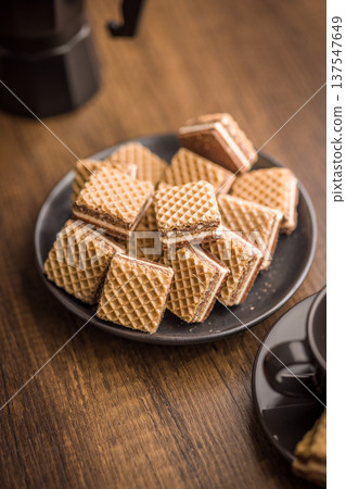 Stack of Chocolate Cream Wafer Cookies on Plate with Coffee Cup in Soft Focus Stack of Chocolate Cream Wafer Cookies on Plate with Coffee Cup in Soft Focus 137547649