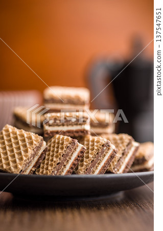 Stack of Chocolate Cream Wafer Cookies on Plate with Coffee Cup in Soft Focus Stack of Chocolate Cream Wafer Cookies on Plate with Coffee Cup in Soft Focus 137547651