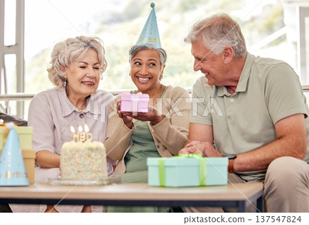Birthday, senior friends with cake and gift for celebration in living room, smile and candles in retirement. Happiness, old people and party with dessert, surprise and elderly man with women on sofa. Birthday, senior friends with cake and gift for celebration in living room, smile and candles in retirement. Happiness, old people and party with dessert, surprise and elderly man with women on sofa. 137547824