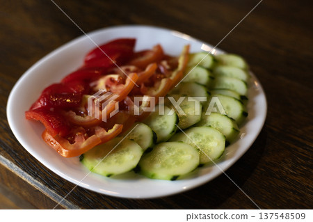 Plate with sliced fresh vegetables including tomatoes cucumber and sweet pepper served on a table Plate with sliced fresh vegetables including tomatoes cucumber and sweet pepper served on a table 137548509