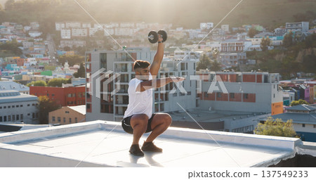 Man, fitness and squat with dumbbell on rooftop in workout, training or outdoor exercise in city. Active male person, athlete or bodybuilder lifting weights on balcony for healthy body or wellness Man, fitness and squat with dumbbell on rooftop in workout, training or outdoor exercise in city. Active male person, athlete or bodybuilder lifting weights on balcony for healthy body or wellness 137549233