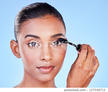 Face, makeup and woman with mascara, brush and beauty with skin glow isolated on blue background. Eyelash extension, cosmetics product and Indian model in portrait with cosmetology in a studio Face, makeup and woman with mascara, brush and beauty with skin glow isolated on blue background. Eyelash extension, cosmetics product and Indian model in portrait with cosmetology in a studio 137549715