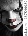 Chilling close up of a terrifying clown with eerie expression and dark background under dim light 137549989