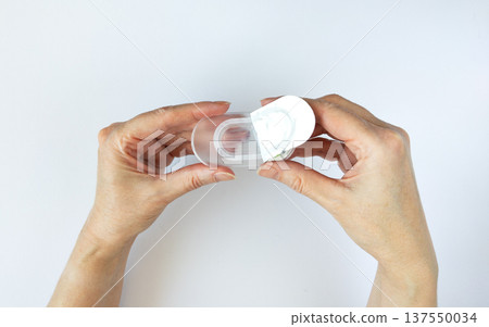 Close-up of hands opening a new package of contact lenses Woman's hands hold an open plastic blister pack containing a contact lens. Close-up of hands opening a new package of contact lenses Woman's hands hold an open plastic blister pack containing a contact lens. 137550034