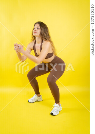 Young woman training doing squats on yellow background Young woman training doing squats on yellow background 137550110