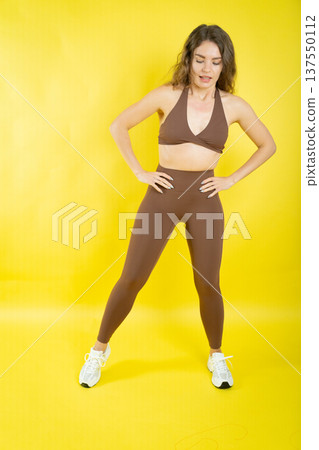 Young woman posing in brown workout clothing against yellow background Young woman posing in brown workout clothing against yellow background 137550112