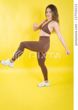 Woman actively exercising wearing brown sportswear on yellow background Woman actively exercising wearing brown sportswear on yellow background 137550131