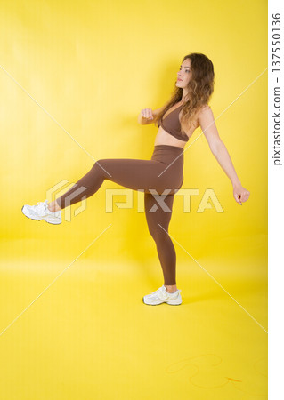 Woman exercising brown sportswear doing a high kick 137550136