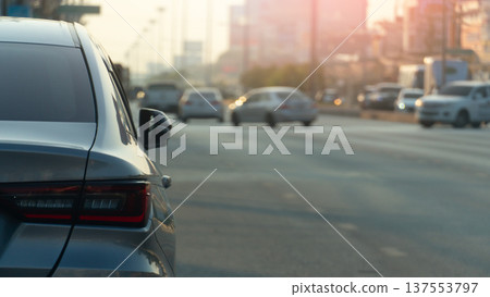 Rear side view of silver car parking beside of asphalt road. Traffic conditions are light and clear. Background of town with many car in the U-Turn. Evokes a soft and relaxing feeling in the morning. 137553797