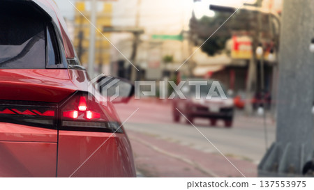 Close up taillight of luxury red car. Blurred light coming from the car from the brake lights. Background of traffic is light in small towns with few cars driving at Thailand. 137553975