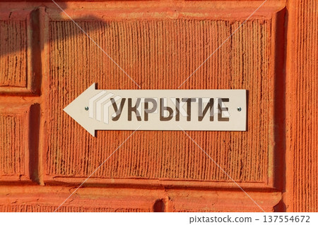 Russian Shelter sign with an arrow pointing left mounted on a rough, bright orange textured building facade in Russia Russian Shelter sign with an arrow pointing left mounted on a rough, bright orange textured building facade in Russia 137554672