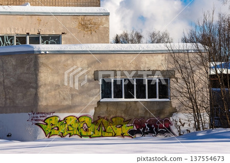 Weathered building facade covered in vibrant graffiti, contrasting with fresh snow and a bright winter sky. Urban decay meets street art in a stark, cold landscape. Russia 137554673