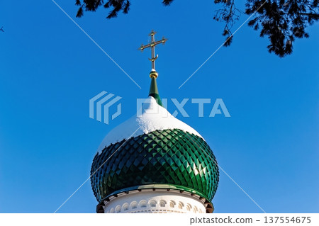 Striking close-up of a green onion dome topped with a golden Orthodox cross, partially covered in white snow against a brilliant blue winter sky Striking close-up of a green onion dome topped with a golden Orthodox cross, partially covered in white snow against a brilliant blue winter sky 137554675