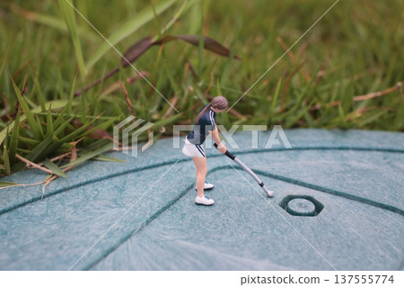 Tiny Figurine Performs Golf Stroke Toward Circular Target Tiny Figurine Performs Golf Stroke Toward Circular Target 137555774