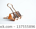 A single metallic copper-colored paper clamp standing upright on a white surface in soft light 137555896