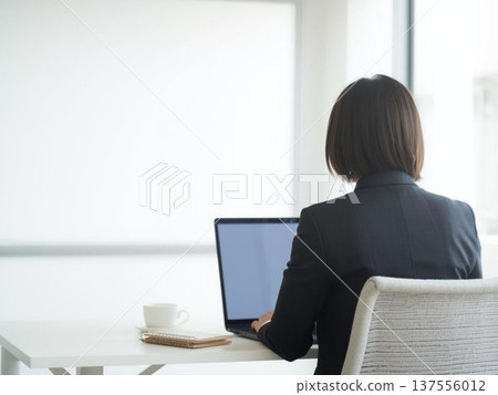 一位女士背對著鏡頭，正在使用筆記型電腦。畫面展現了辦公室工作和遠距辦公的場景。 137556012
