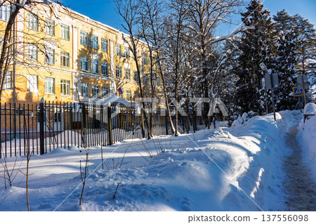 Sunny winter day facade of a classic Russian school building with snow-covered grounds and bare trees. Russia Sunny winter day facade of a classic Russian school building with snow-covered grounds and bare trees. Russia 137556098