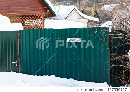 Vibrant green fence with Tsoi's Dead End sign, standing out against crisp white snow in a peaceful winter dacha community. Russia Vibrant green fence with Tsoi's Dead End sign, standing out against crisp white snow in a peaceful winter dacha community. Russia 137556117