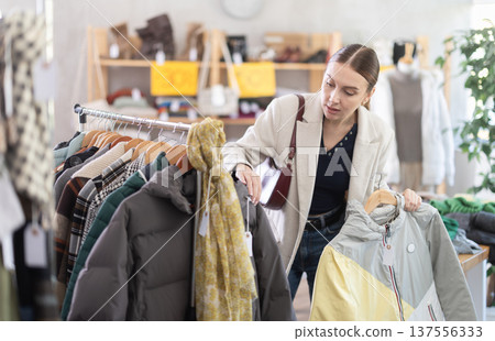 Attentive young woman choosing down jacket in clothing store 137556333