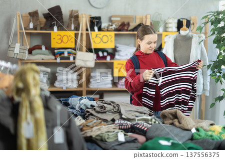 Teenage girl chooses sweater in clothing store Teenage girl chooses sweater in clothing store 137556375