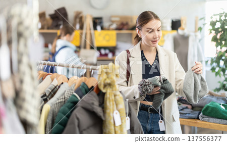 Focused european young woman choose hat on Black Friday sale of winter clothing collection in clothing store Focused european young woman choose hat on Black Friday sale of winter clothing collection in clothing store 137556377