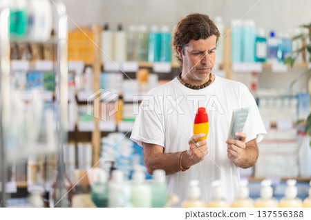 Adult man chooses sunscreen at pharmacy Adult man chooses sunscreen at pharmacy 137556388