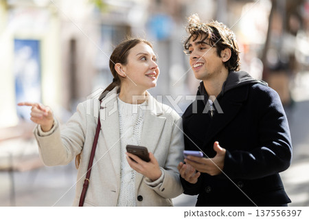 Friendly couple of tourist strolling through summer city streets and pointing at sights 137556397