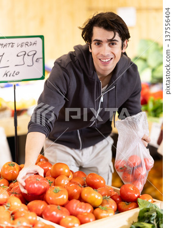 Man selects red tomatoes in the produce section of a supermarket. Names of vegetables in Spanish Man selects red tomatoes in the produce section of a supermarket. Names of vegetables in Spanish 137556404