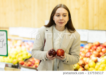 Positive woman chooses ripe apples for purchase in greengrocer shop 137556517