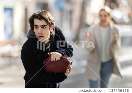 Young man snatching handbag from woman on street Young man snatching handbag from woman on street 137556518