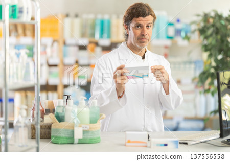 Adult male pharmacist working at computer and offering pills 137556558