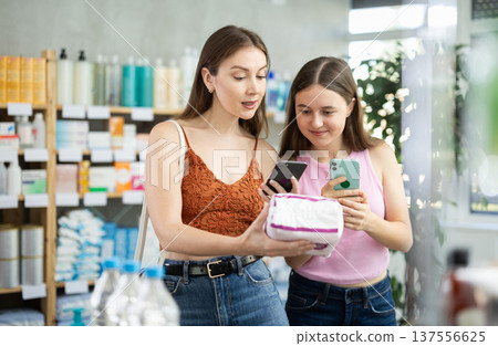 Mom and daughter scan a package with pads on their phone at a pharmacy Mom and daughter scan a package with pads on their phone at a pharmacy 137556625