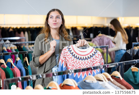 Smiling female in casual outfit admiring pullover with a pattern in a showroom 137556675
