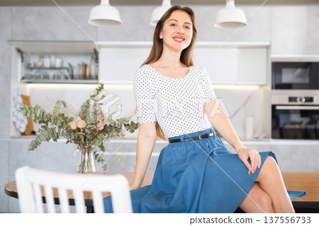 Smiling middle-aged woman posing sitting on kitchen table 137556733