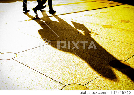 A shadow of a person stretching out in the light of the setting sun and his feet walking 137556740