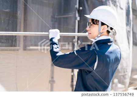 A scaffolder wearing glasses working at a large-scale repair construction site 137556749