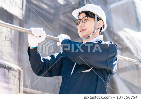 A scaffolder wearing glasses working at a large-scale repair construction site 137556754